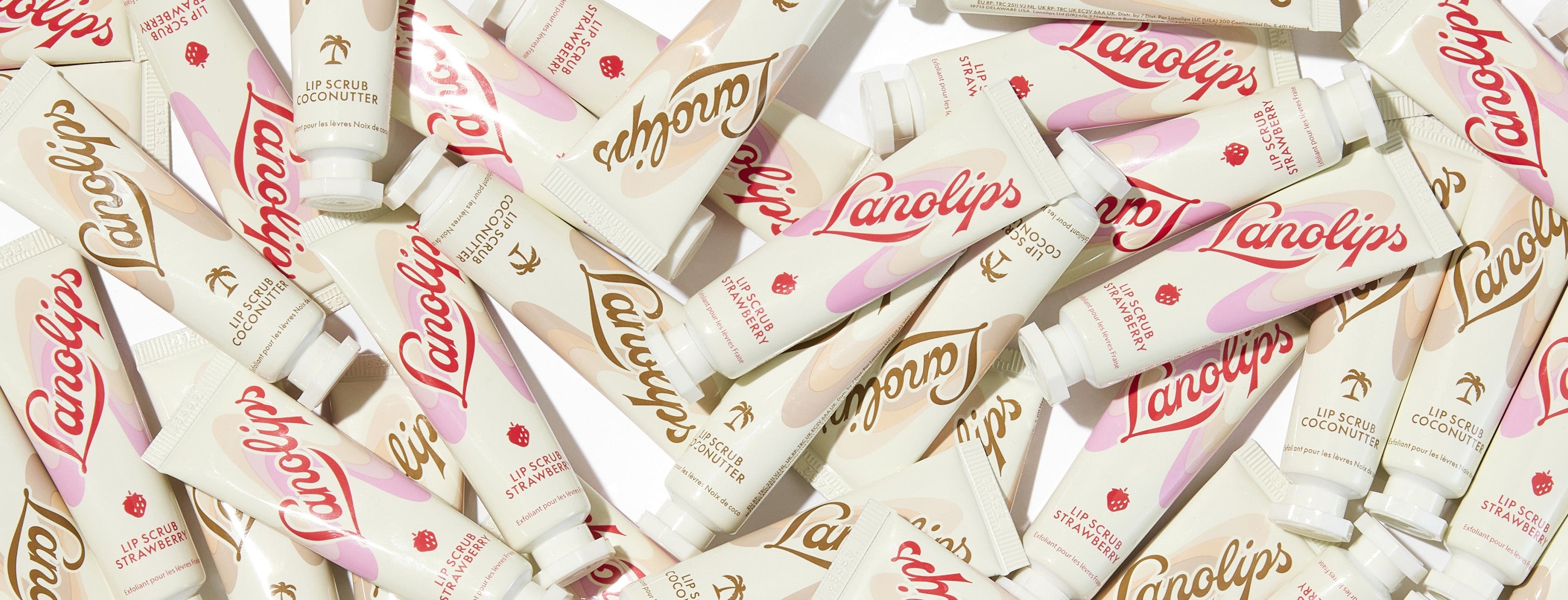Photo containing multiples tubes of Lanolips Lip Scrubs in Coconutter and Strawberry scattered in a white background.
