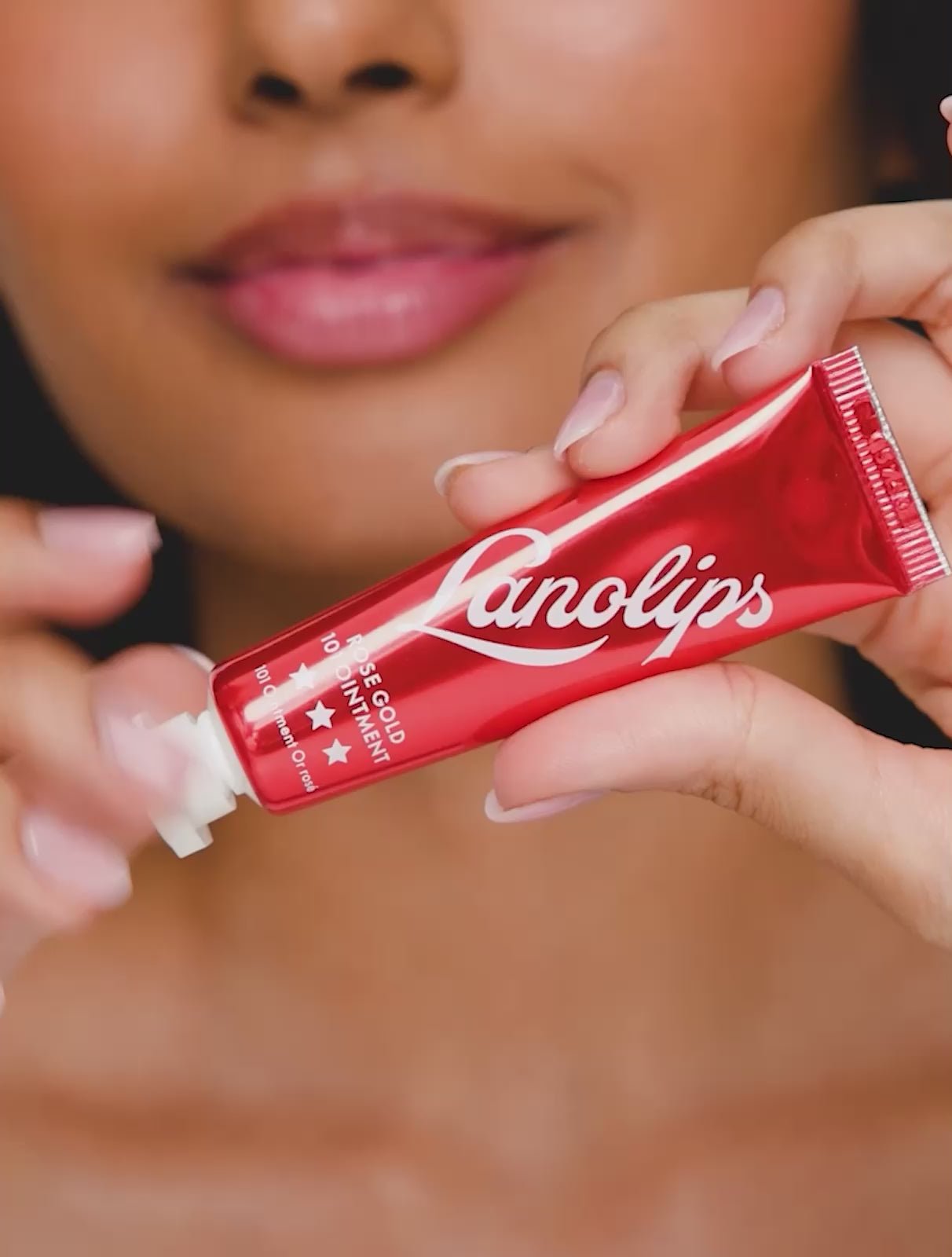 A video of a model applying and wearing Lanolips Rose Gold 101 Ointment, unveiling a dense, rich rose gold tint that enhances lips and cheeks with a natural, flushed glow. The ultra-hydrating formula delivers a dewy, non-sticky finish, mimicking the effect of blood rushing to the skin for a healthy, radiant look.
