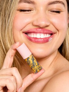 Model smiling while holding Lanolips Hyaluronic Lip Oil Honey, showing glossy, hydrated lips with a radiant finish