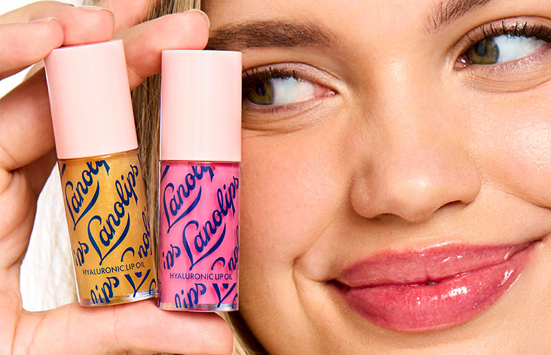 Close up shot of a model holding the Lanolips Hyaluronic Lip Oil on the side of her face. Comes in two shades: Honey and Raspberry