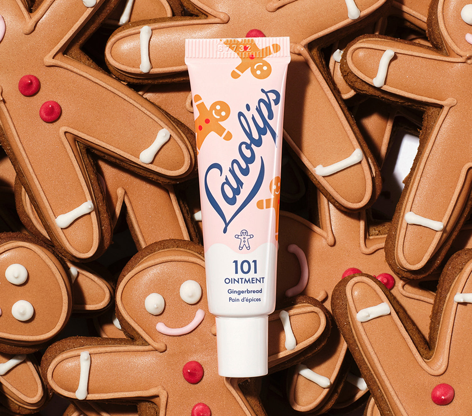 A tube of Lanolips 101 Ointment Multi-Balm Gingerbread lip balm surrounded by gingerbread cookies. Made with all-natural lanolin, vitamin e and infused with warm spice. 