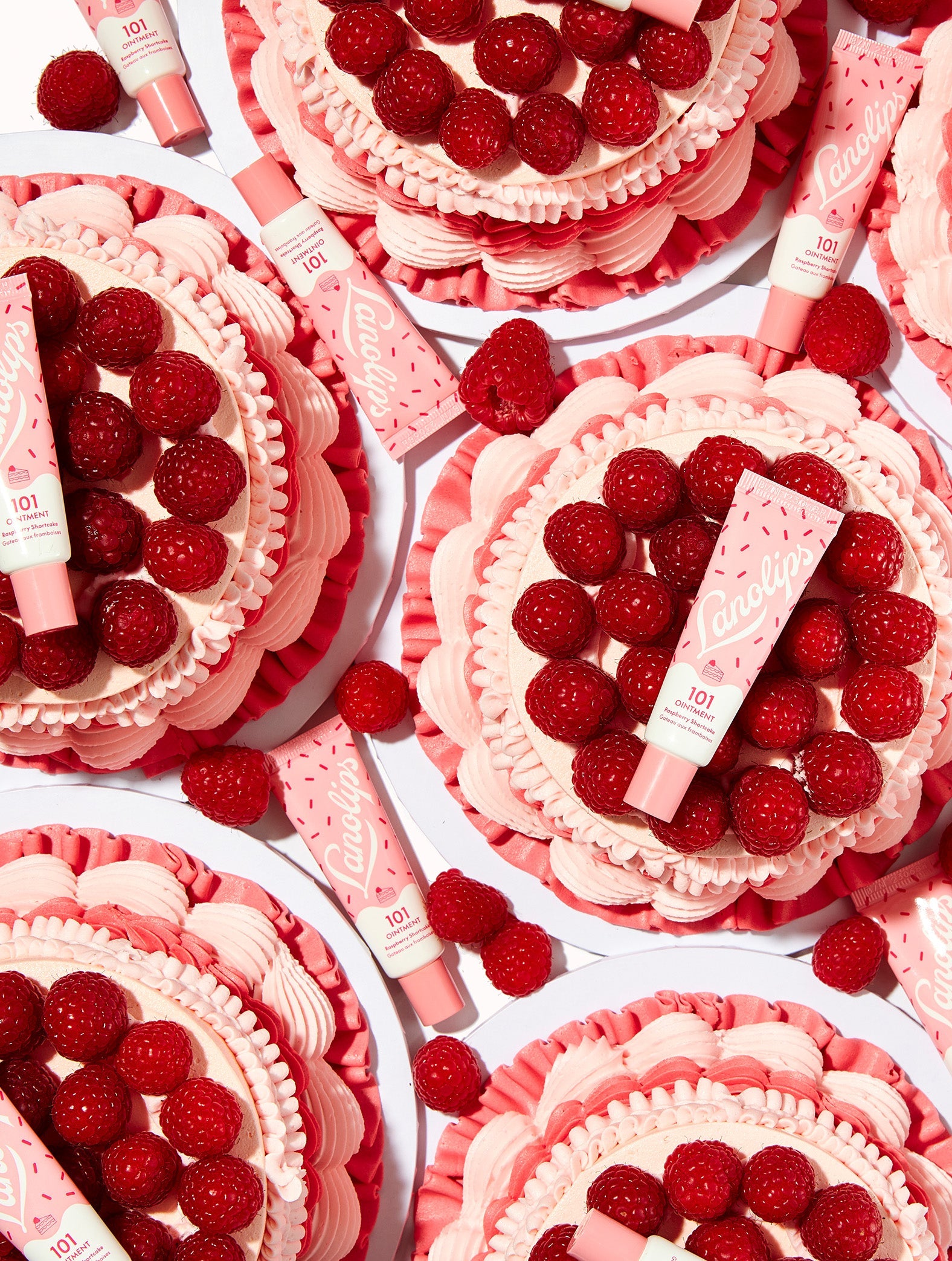 Flat lay of multiple Lanolips 101 Ointment Multi-Balm Raspberry Shortcake sitting on top of vintage styled raspberry shortcakes. With added berry sweetness to your pout, with one swipe of pure Lanolin goodness, Vitamin E and Natural Raspberry Flavour.
