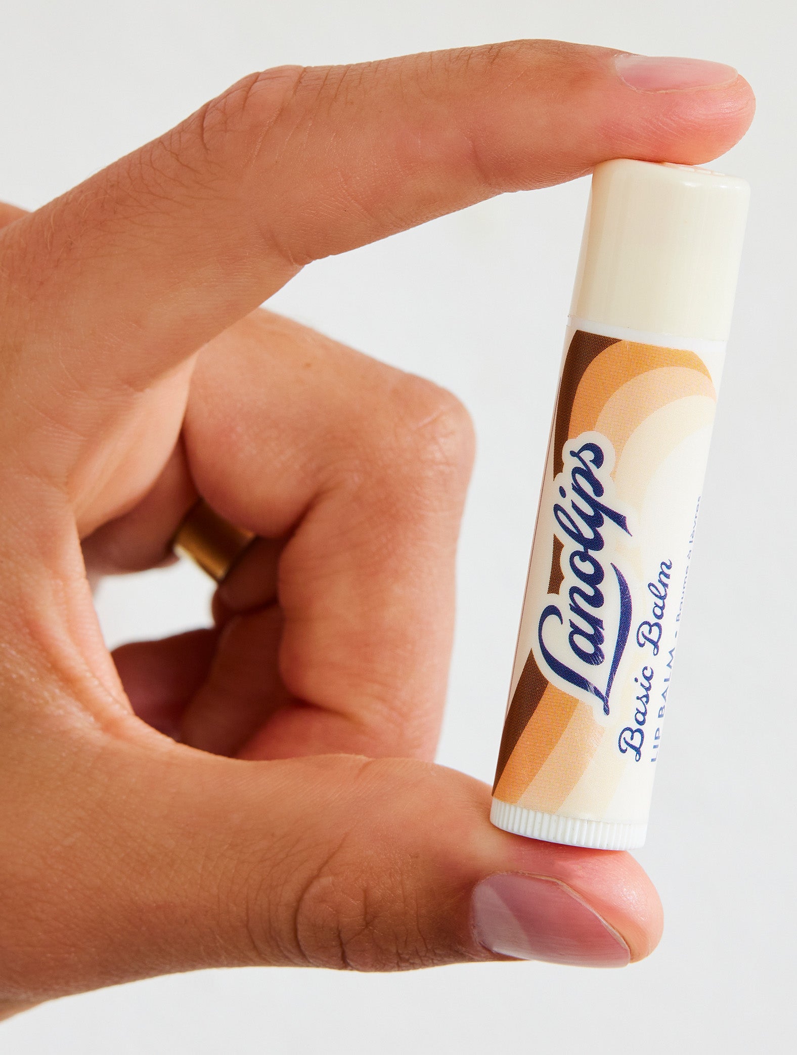 Hand holding a Lanolips Basic Balm Coconutter against a white background