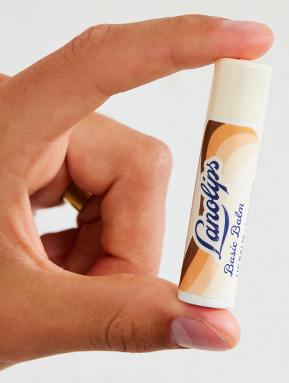 Hand holding a Lanolips Basic Balm Coconutter against a white background