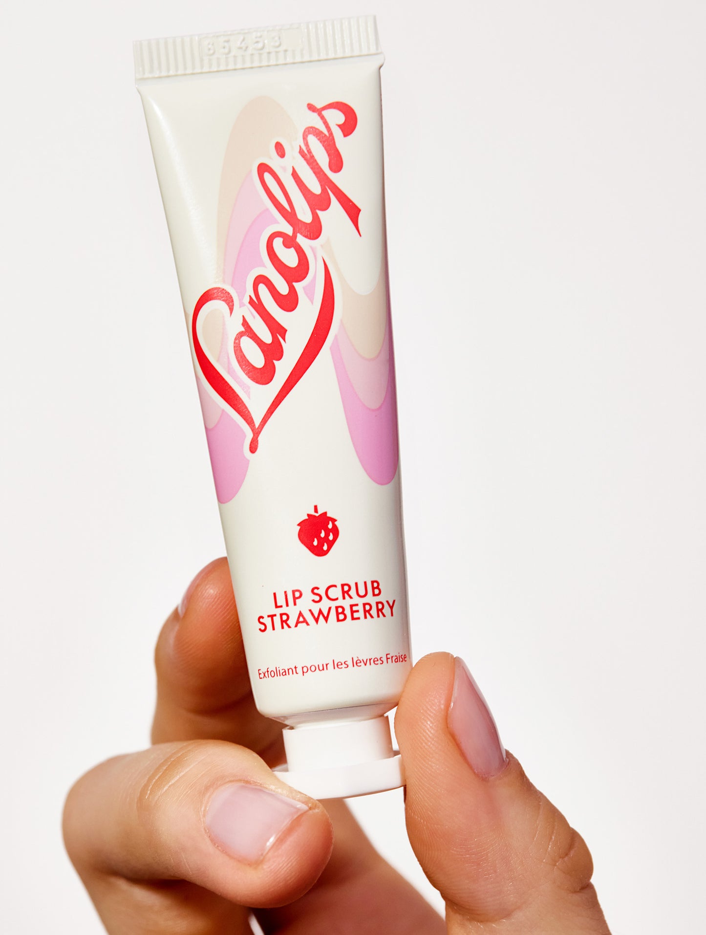 Model's hand holding a lanolips lip scrub in strawberry against a white background.