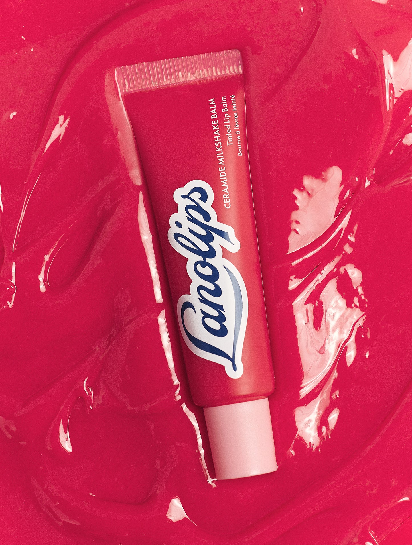 Lanolips Milkshake Ceramide Balm in Raspberry Crumble on glossy raspberry balm texture background, showing sheer creamy tint
