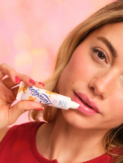 Model applying Lanolips 101 Ointment Multi-Balm Gingerbread lip balm to her lips with a pink background. Embrace warm spice and soft lips with this limited edition festive 101 Delicious Holiday gourmand flavour. 